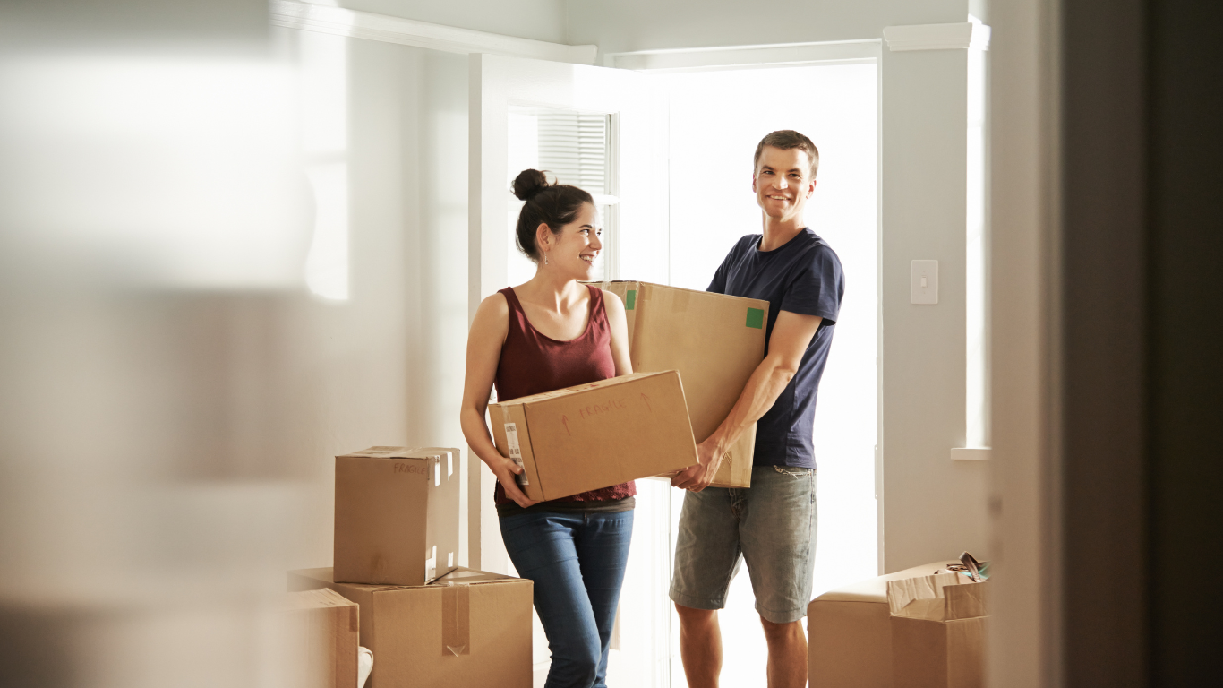 Happy first-time buyers moving in to their first home holding boxes