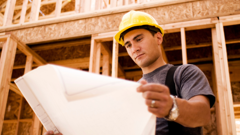 Self-employed Liverpool builder on site wearing PPE, reviewing plans—CIS contractor working in Merseyside